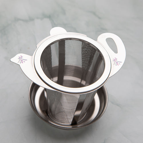 Stainless steel tea strainer with a teapot shaped lid marked with the character for tea, on a drip dish, by Bettina's Tea
