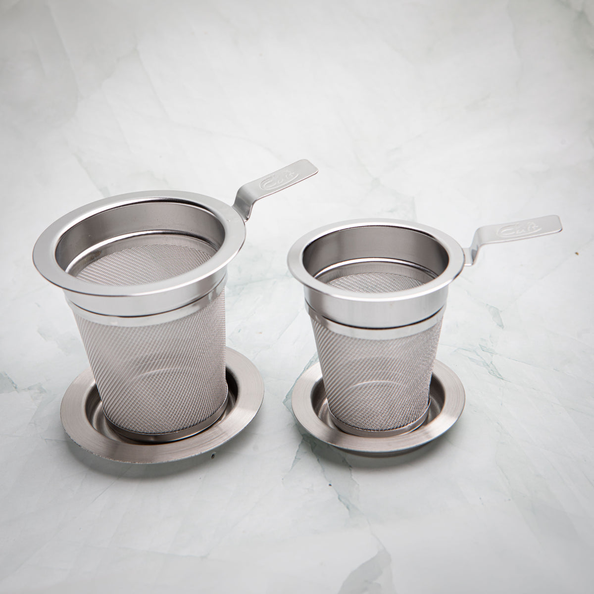 Two stainless steel tea strainers, sizes M and S, each with a flat handle and a dish, by Bettina's Tea